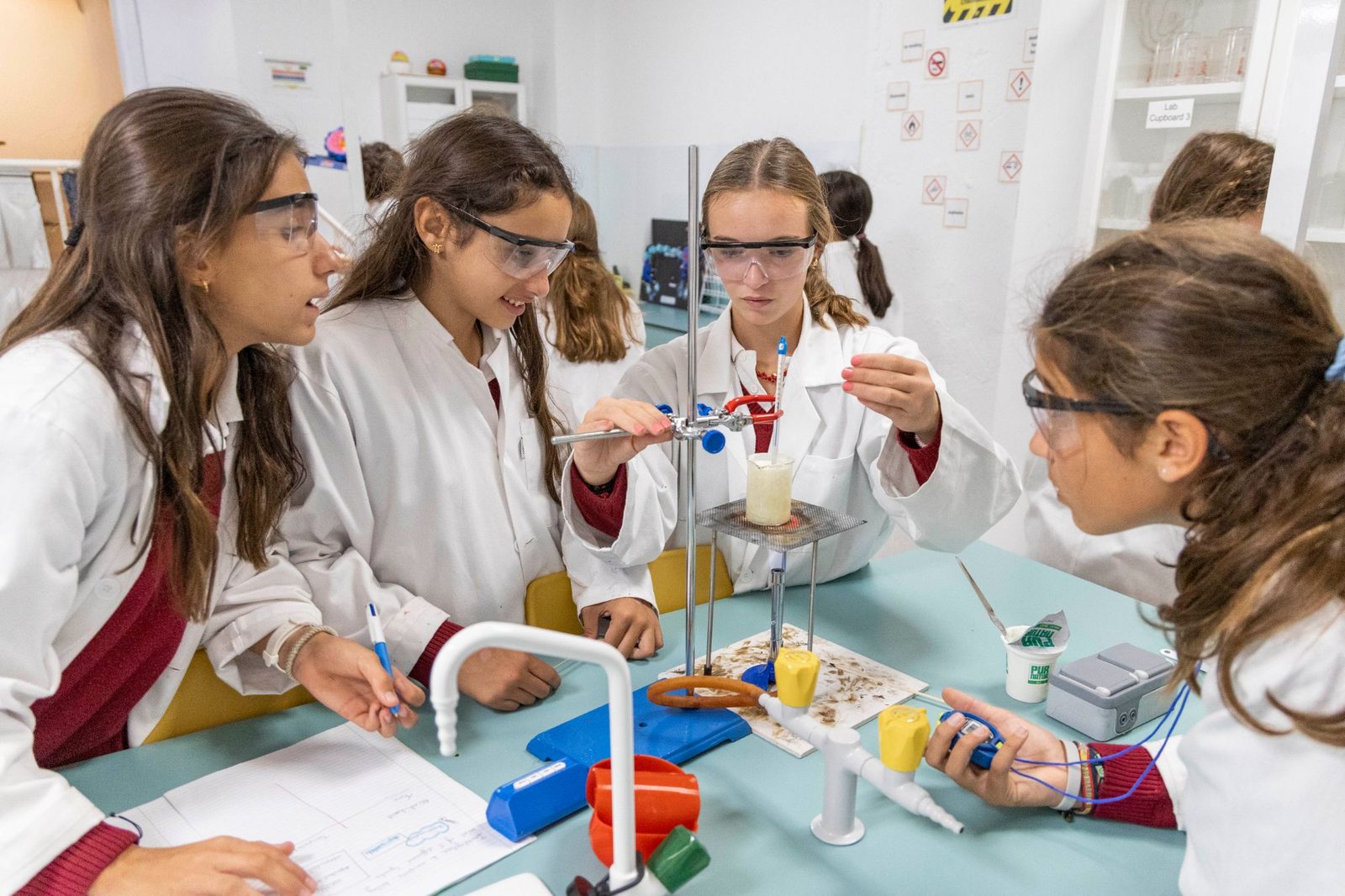 Alumnas con bata y gafas de seguridad realizando un experimento en el laboratorio de ciencias de Dallington School