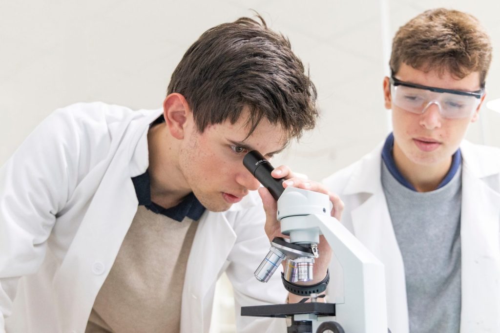 Dos alumnos con bata de laboratorio usando un microscopio en Dallington School