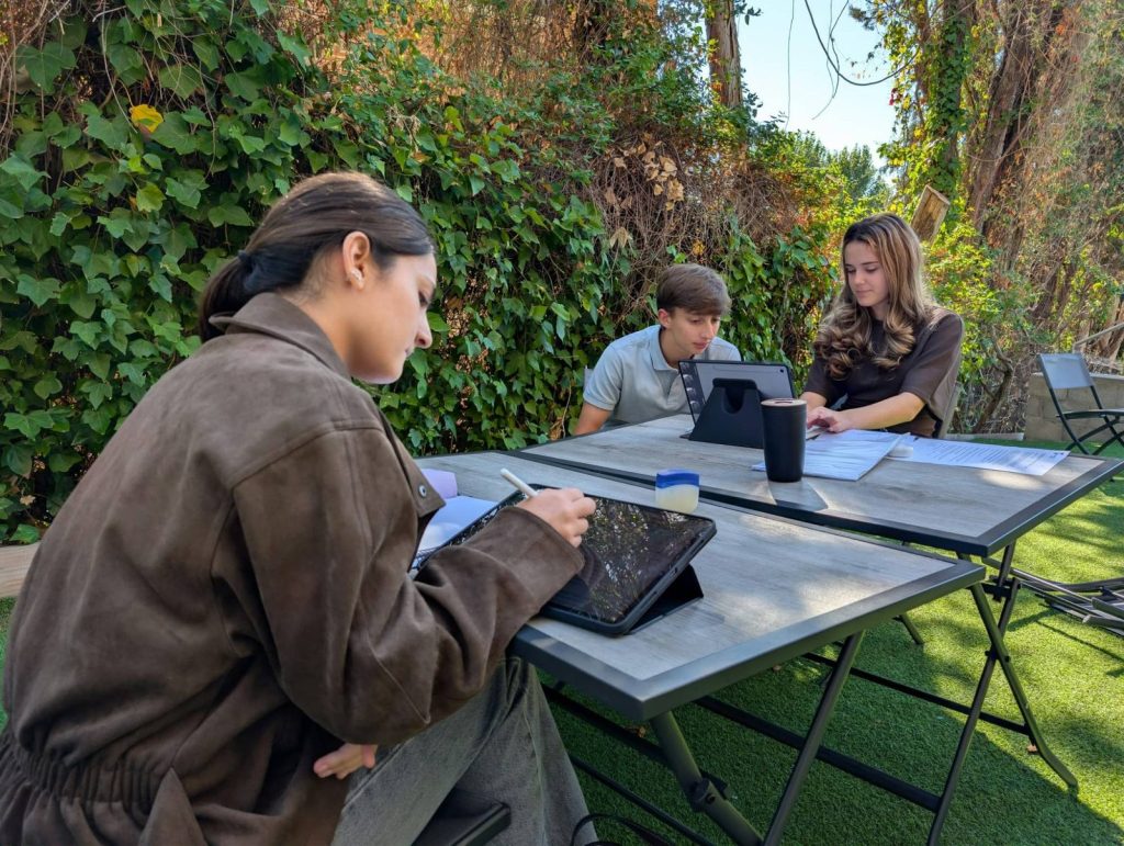 Tres alumnos trabajando en un proyecto con tablets y documentos en el jardín de Dallington School