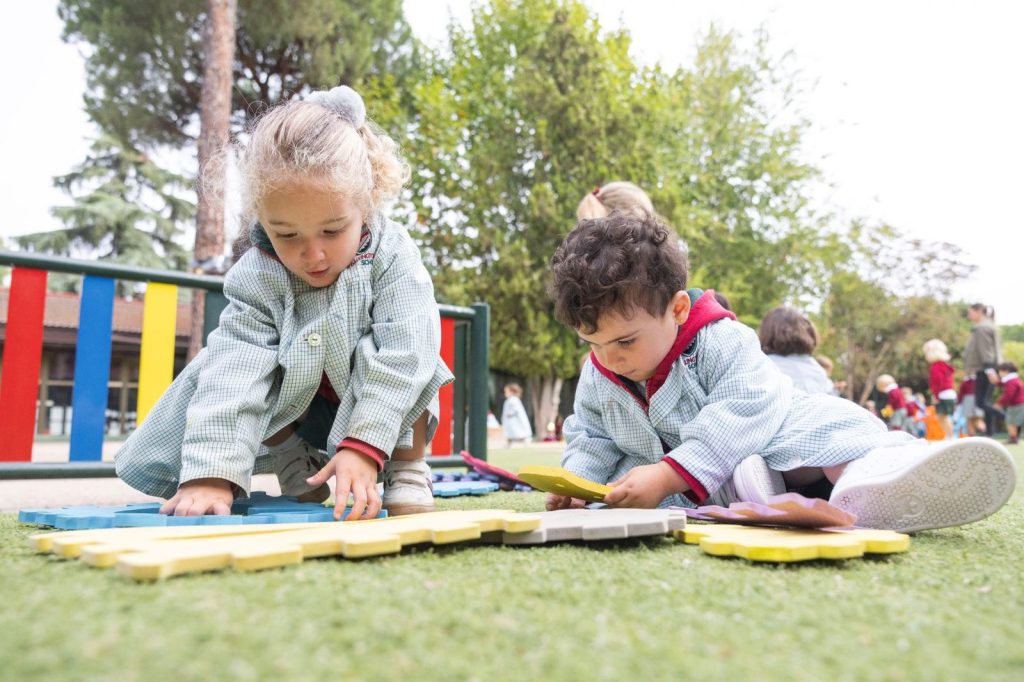 Dos niños pequeños construyendo con piezas de colores sobre el césped del patio de Dallington School