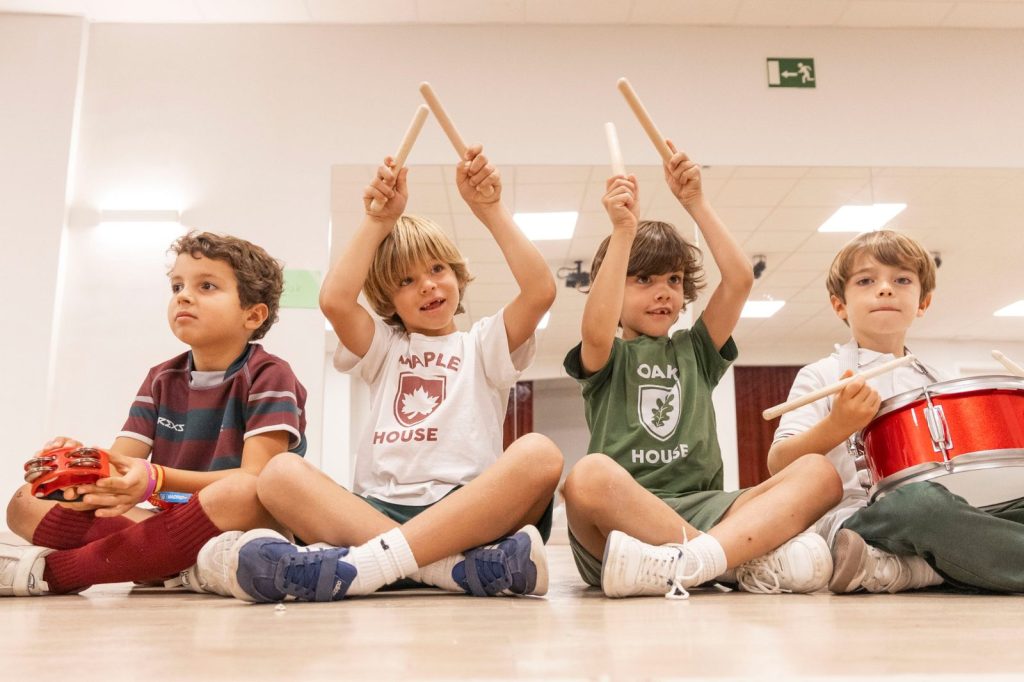 Cuatro niños sentados en el suelo con instrumentos de percusión durante una actividad de música en Dallington School